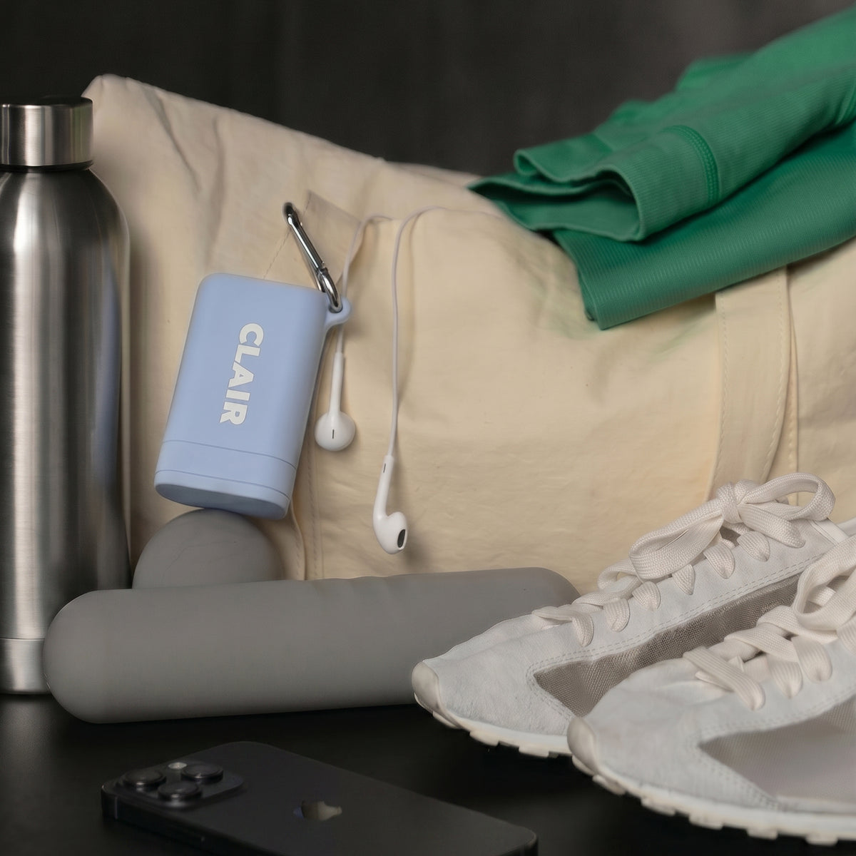 CLAIR case in Sky clipped to a canvas gym bag beside a water bottle, foam roller, earbuds and sneakers